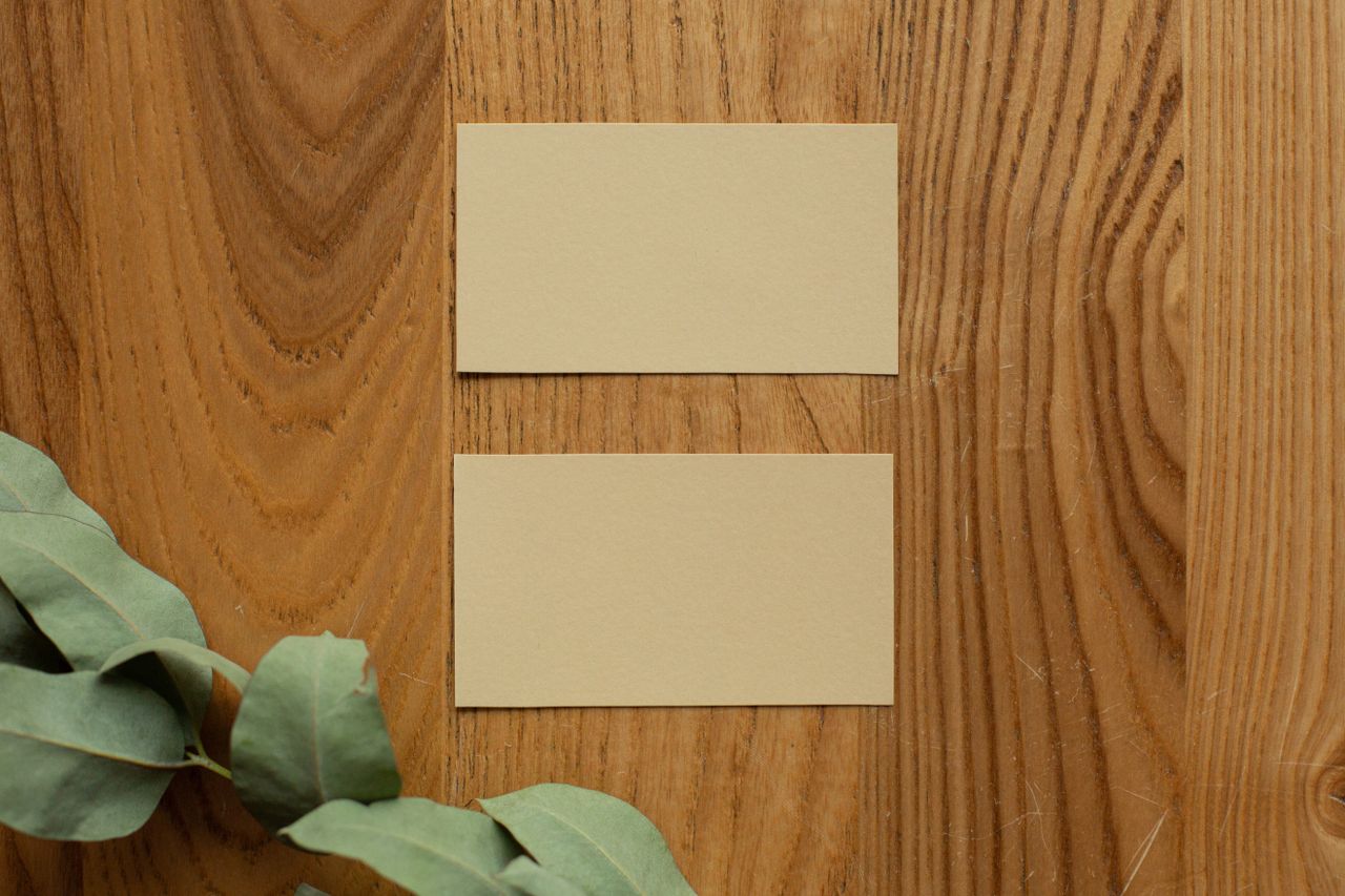 Top view of mock up yellow business cards placed on wooden surface near plant with green leaves in light room